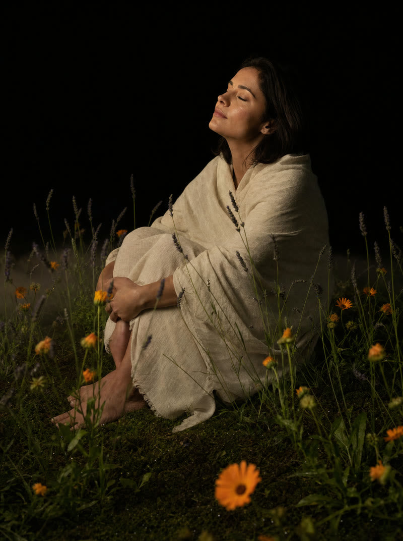 A woman seated at rest in a night garden, botanicals catching a warm key light